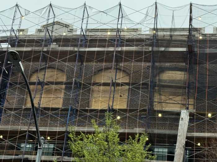 close up of scaffolding outside brick school building with windows boarded over