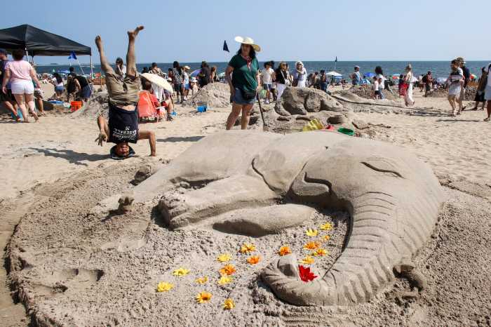 Tony Cusicanqui doing a headstand next to sand elephant sculpture